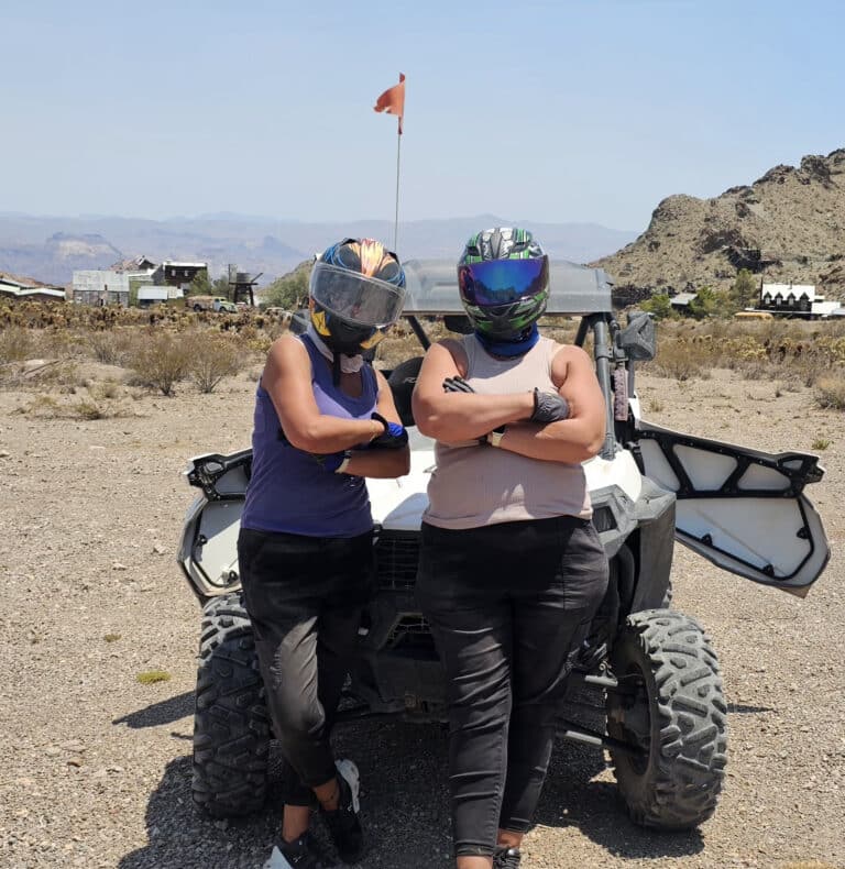 Two adventurers in helmets and sunglasses pose by an ATV near Las Vegas for a thrilling RZR off-road ride in the Nevada desert.