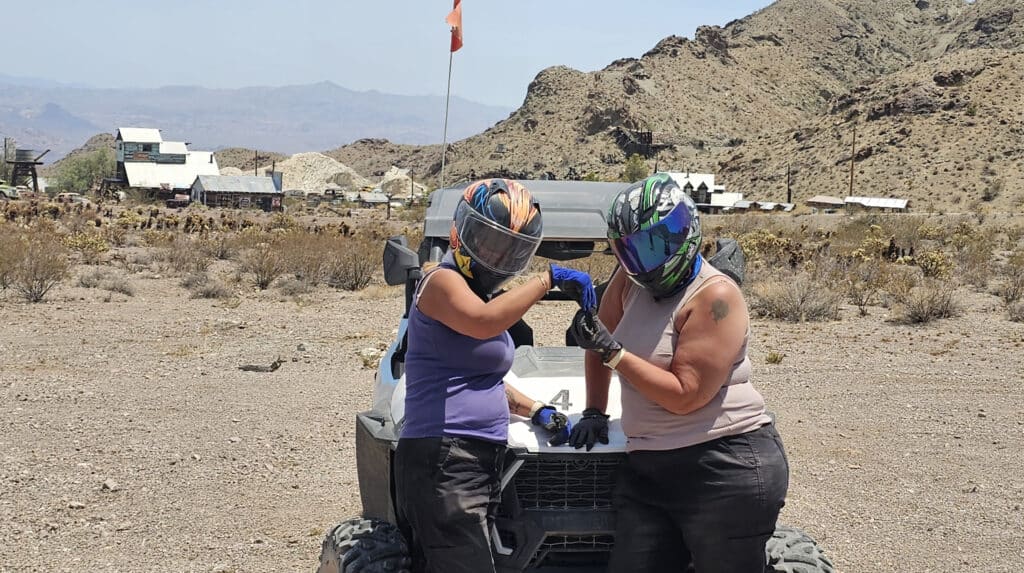 Adventurers in helmets and gloves pose by an ATV in Nevada desert near Las Vegas, ready for RZR off-road tours and Ghost Town fun.