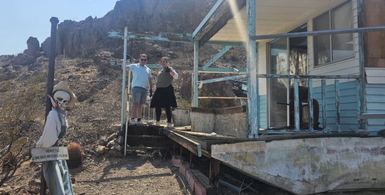 Two people on a rustic blue porch in a Nevada ghost town near Las Vegas; skeleton decor & signpost, perfect for sightseeing & ATV tours.