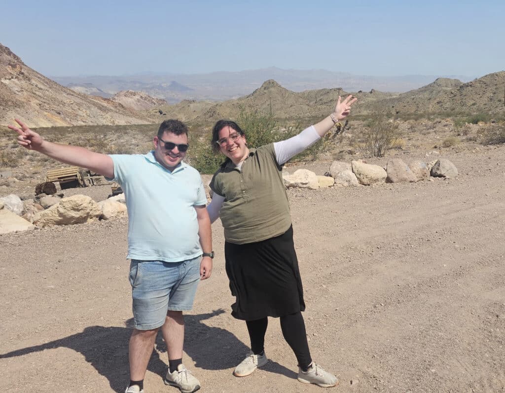 Two friends flash peace signs on a Nevada desert trail near Las Vegas, enjoying an ATV tour by the Colorado River’s rocky hills.