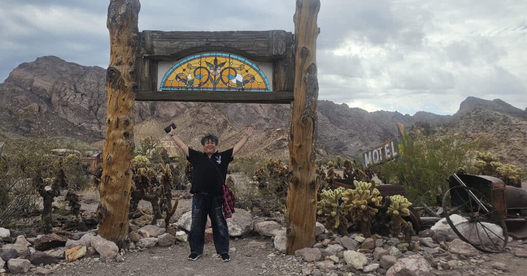 Smiling under a rustic stained-glass arch in a Nevada desert near Las Vegas, with cacti and old MOTEL sign—perfect for ATV tours!.