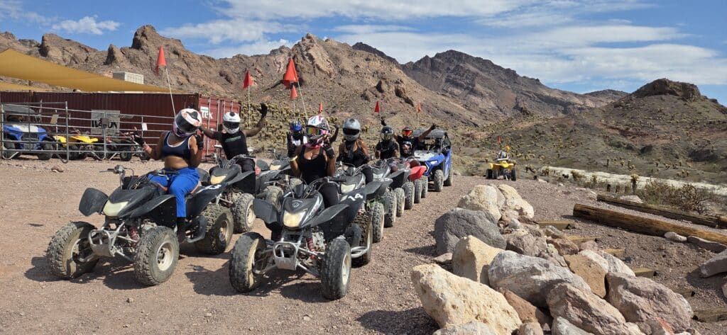 Adventurers in helmets line up on black ATVs for a Las Vegas desert tour near the Colorado River, Nevada—red safety flags flying.