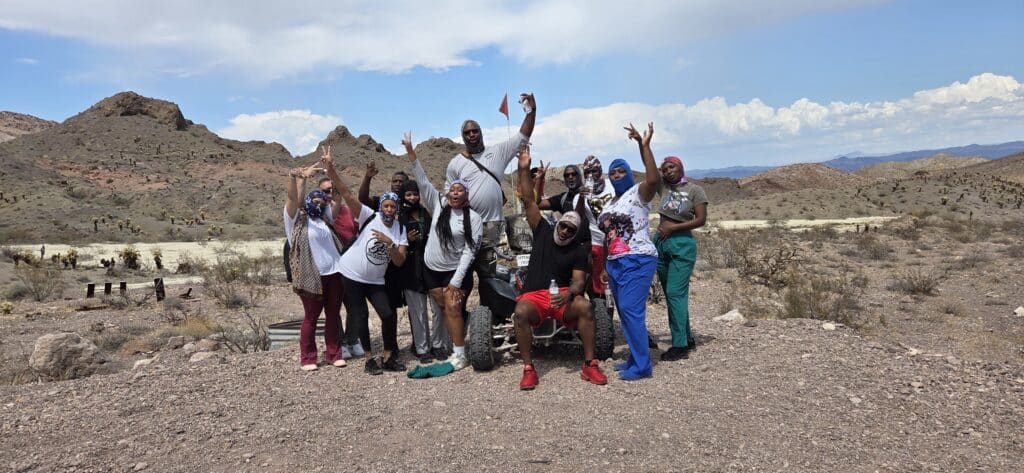 Energetic group poses on Nevadas rocky desert near Las Vegas, smiling after thrilling RZR off-road and Ghost Town tour.