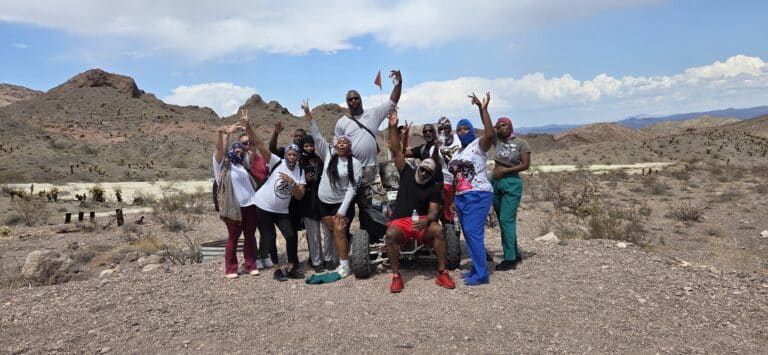 Energetic group poses on Nevadas rocky desert near Las Vegas, smiling after thrilling RZR off-road and Ghost Town tour.