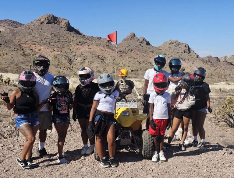 Group enjoying an ATV tour near Las Vegas, Nevada, posing by a yellow RZR in the desert with cacti and mountain views.