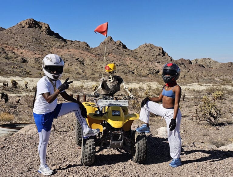 Three adventurers in helmets pose with a yellow ATV in the Nevada desert near Las Vegas, ready for an exciting ATV tour.