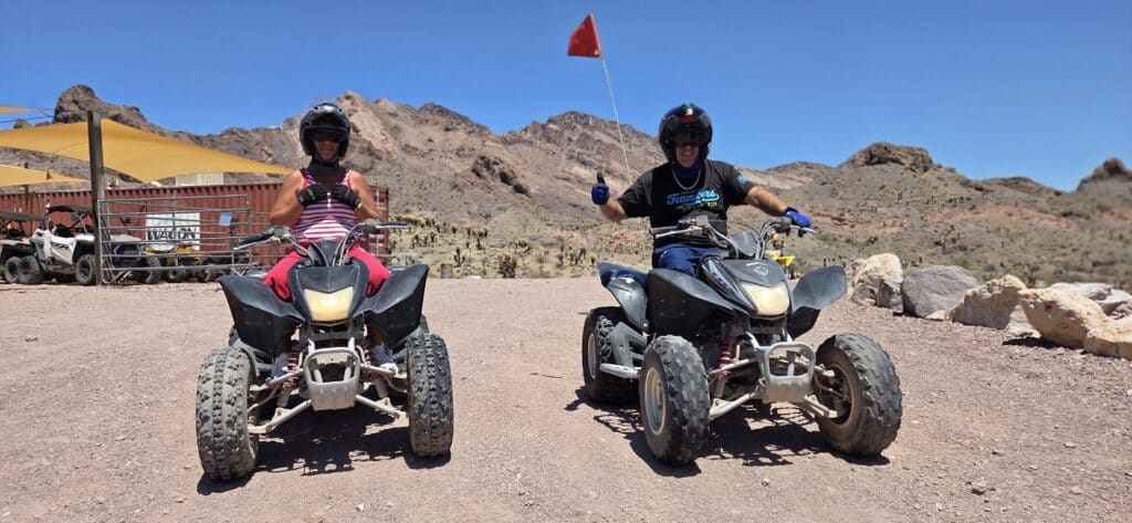 Riders in helmets and gloves enjoy an ATV tour near Las Vegas, Nevada, with rocky desert hills and a Colorado River backdrop.
