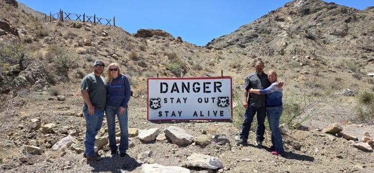 Four adults pose by a “DANGER STAY OUT STAY ALIVE” sign near Las Vegas, Nevada, during an ATV tour by the Colorado River.