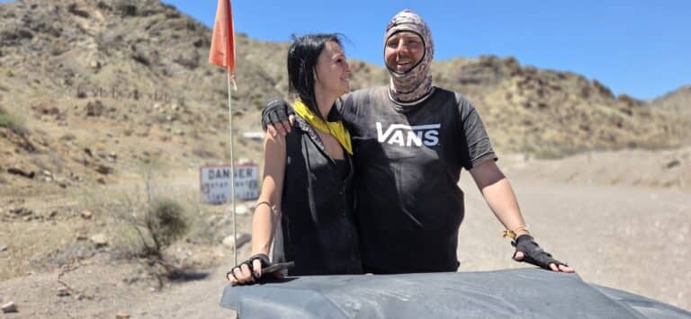 Smiling friends after an ATV tour near Las Vegas, Nevada, pose by rocky hills and a DANGER sign on a dusty RZR adventure.