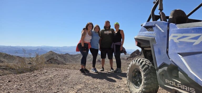 Four friends smile on a Nevada hilltop near Las Vegas, with a Polaris RZR after an epic ATV tour along the Colorado River.