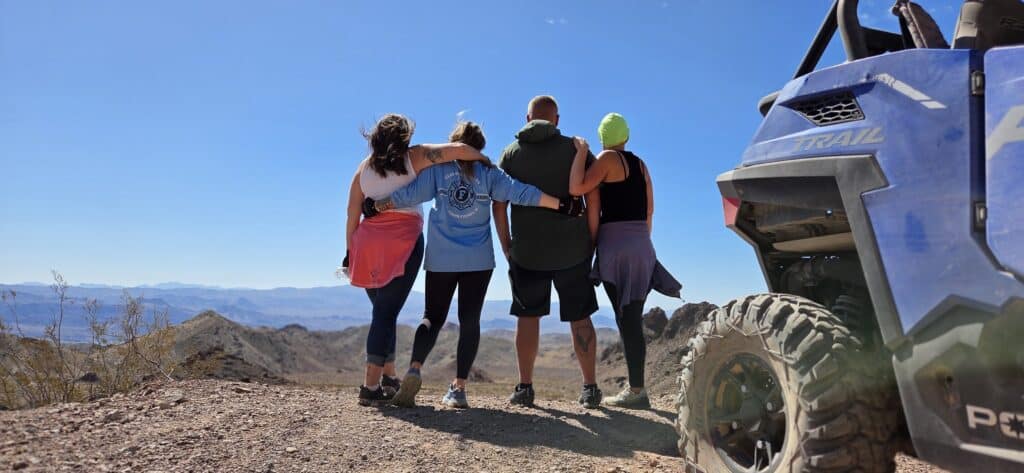 Friends stand arm in arm at a Nevada overlook by their RZR after an epic Las Vegas ATV tour near the Colorado River.