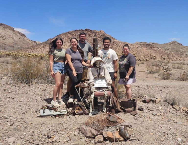 Five friends pose by a skeleton in Nevada’s rocky desert near Las Vegas during a ghost town ATV tour by the Colorado River.
