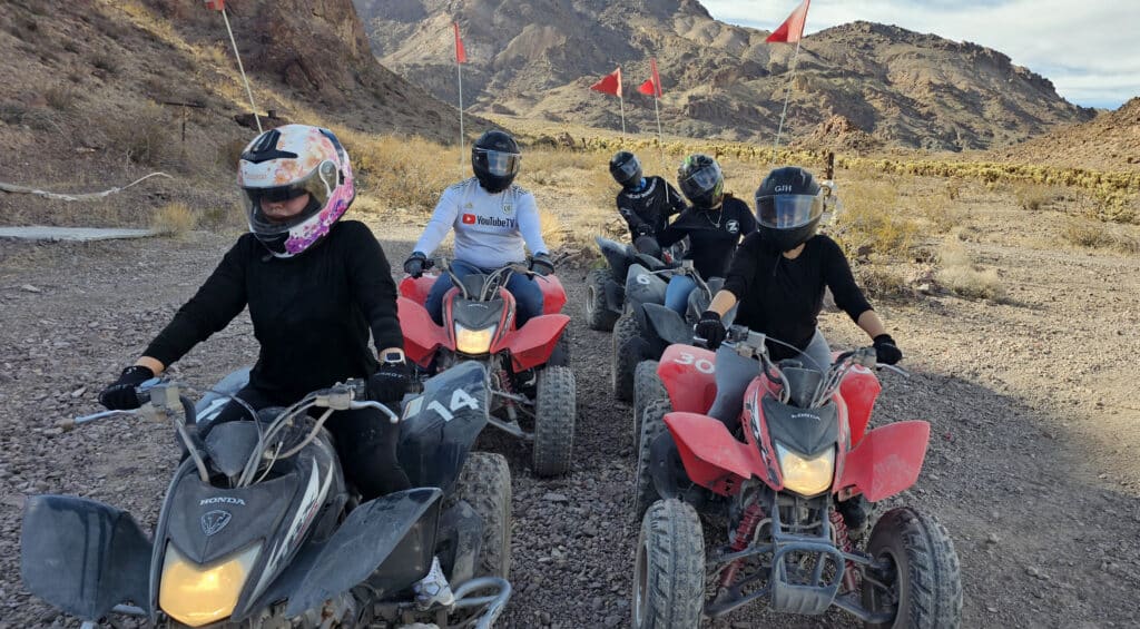 Riders in helmets enjoy a thrilling ATV tour near Las Vegas, Nevada, on a rocky desert trail with scenic mountain views.