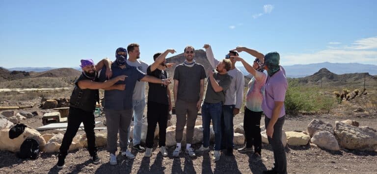 A cheerful group poses playfully near Las Vegas in a Nevada desert, enjoying RZR off-road rides under a clear blue sky.