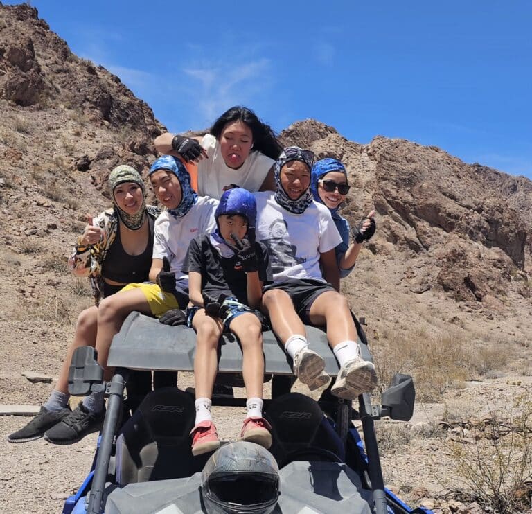 Group enjoys a playful RZR off-road ride near Las Vegas, Nevada, posing atop their vehicle in the rocky desert under blue skies.