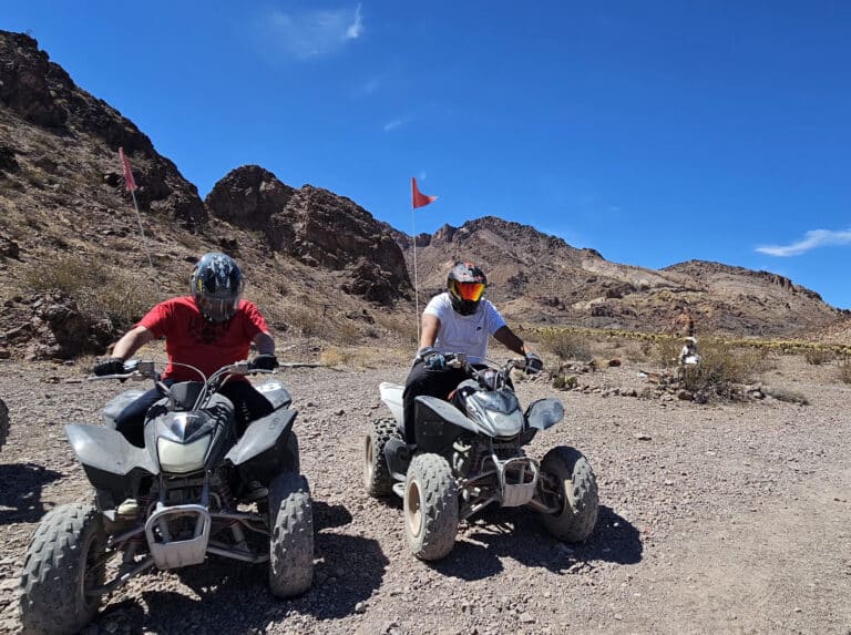 Experience a thrilling ATV tour near Las Vegas, Nevada, riding quad bikes on rocky desert trails with mountain views and red flags flying.