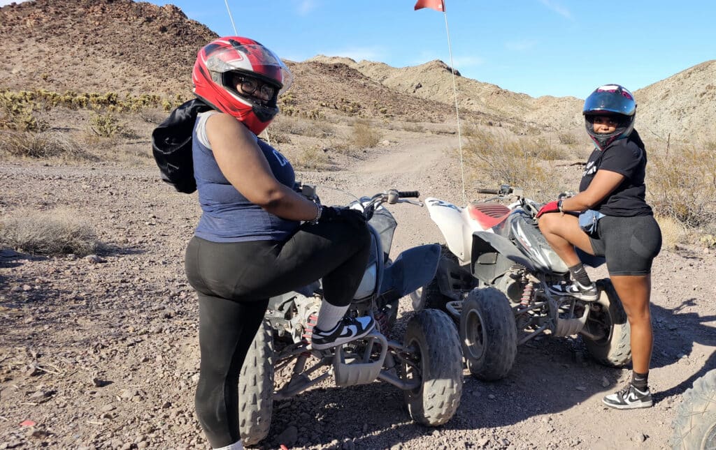 Two women in helmets pose by ATVs on a Nevada desert trail near Las Vegas—perfect for ATV tours and RZR off-road adventures.