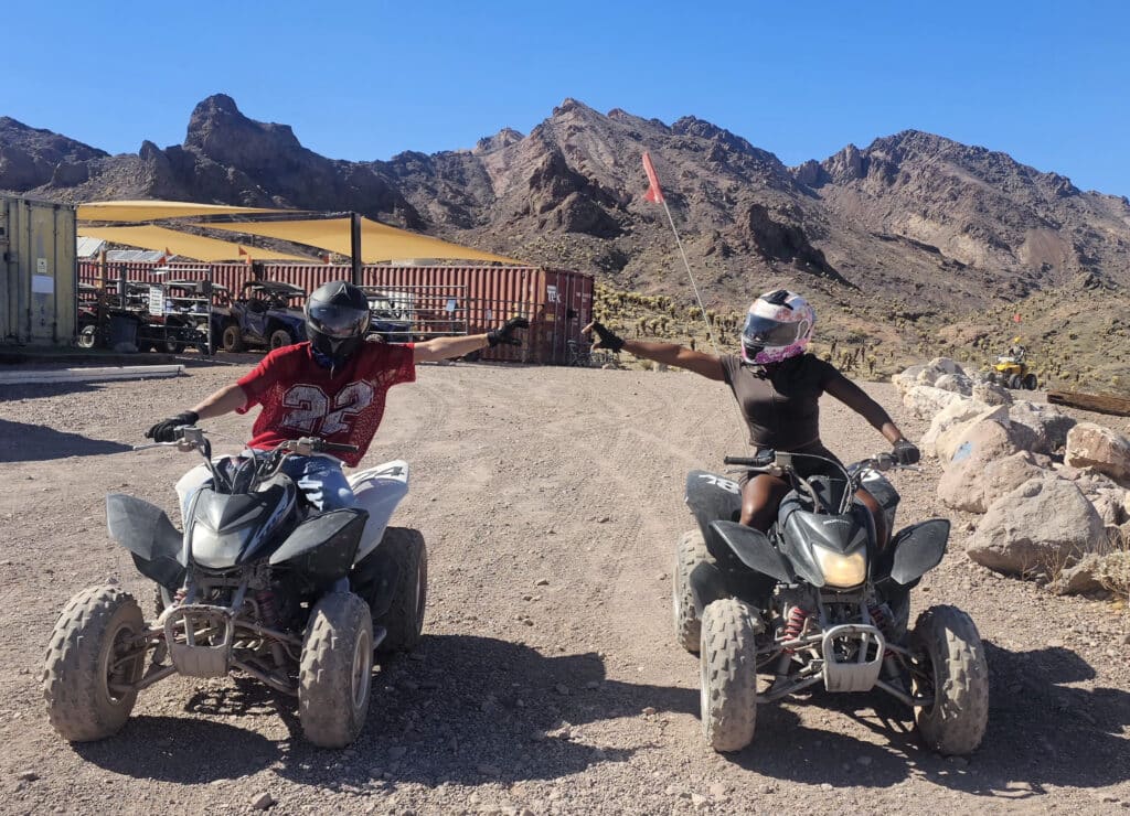 Riders in helmets fist bump on ATVs during a thrilling Las Vegas RZR off-road tour near the Colorado River in Nevada.
