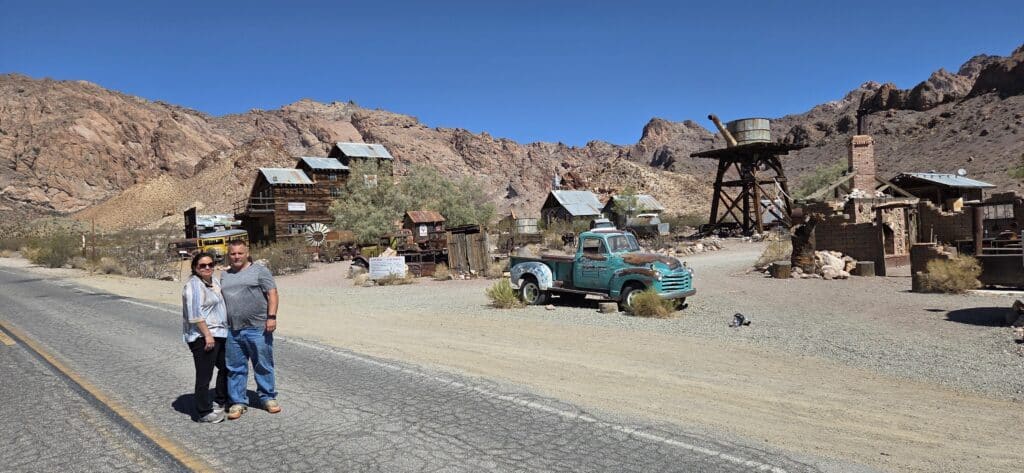 Couple at Nevada ghost town near Las Vegas—rustic wooden buildings, antique truck, and Colorado River ATV tours nearby.