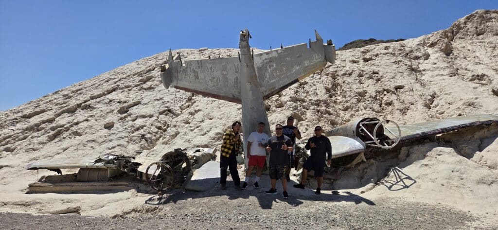 Five adventurers pose by a weathered airplane wreck in Nevada’s desert near Las Vegas, perfect for ATV tours and RZR rides.