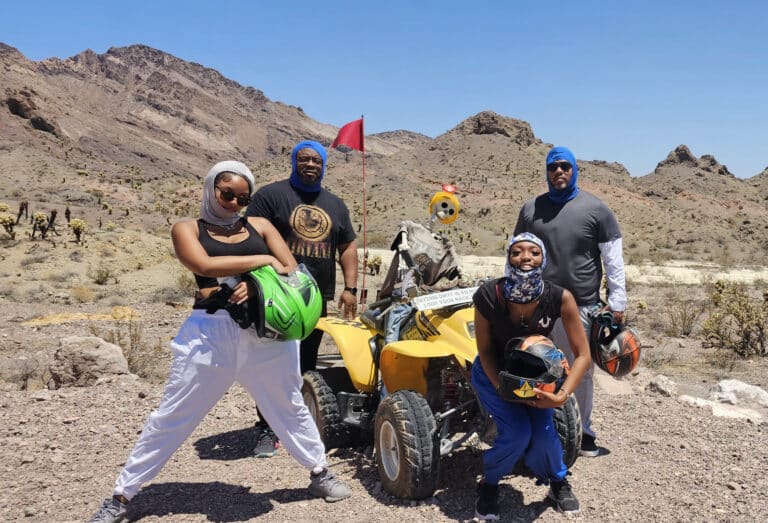 Adventurers in desert gear pose by a yellow ATV near Las Vegas, Nevada, ready for an exciting ATV tour amid cacti and rocky cliffs.