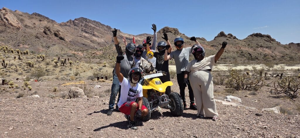Adventure-seekers in helmets celebrate by a yellow ATV in Nevadas desert near Las Vegas on a thrilling ATV tour with mountain views.