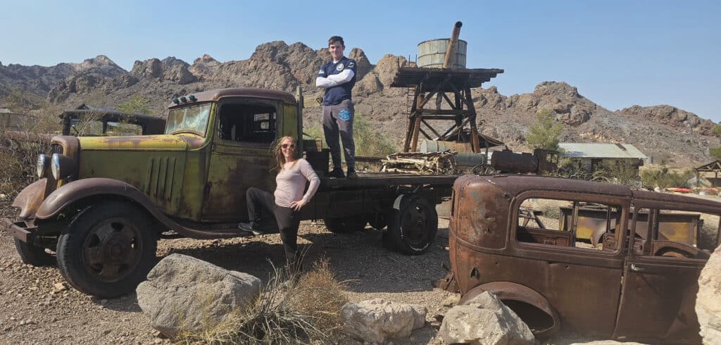 A woman poses by a rusty truck in a Nevada ghost town near Las Vegas; rocky desert views perfect for ATV tours and RZR adventures.