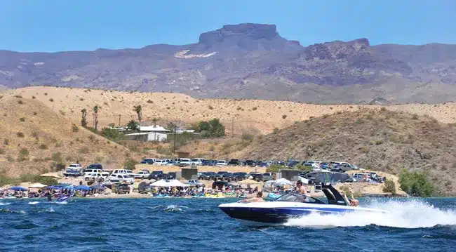 A speedboat races on the Colorado River near Las Vegas, Nevada, past a lively beach with desert hills—perfect for ATV and RZR tours.