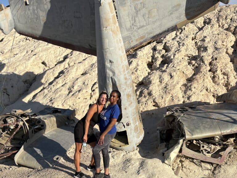 Two women smile by a plane wreck in the Nevada desert near Las Vegas—perfect for ATV tours and Ghost Town sightseeing.