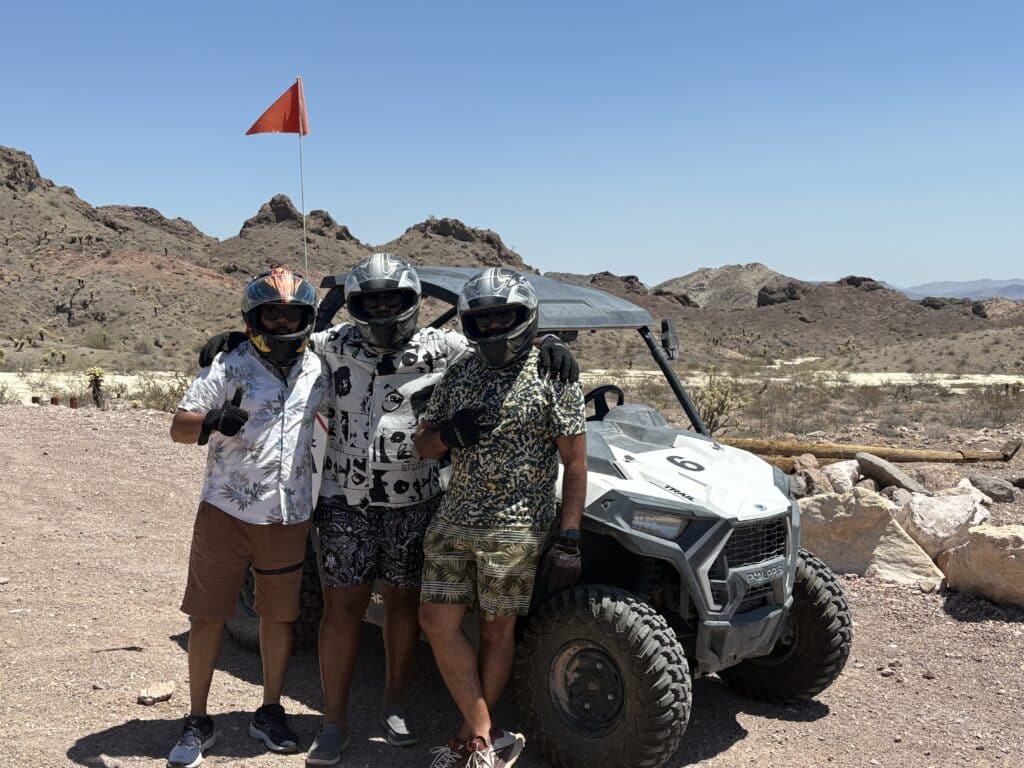 Three adventurers in helmets pose by an ATV in Nevada’s desert near Las Vegas, ready for a thrilling RZR off-road tour.