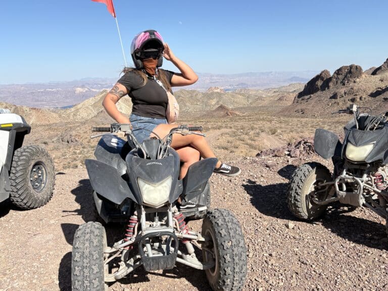 A woman adjusts her helmet on a black ATV in the Nevada desert near Las Vegas, ready for an exciting ATV tour adventure.