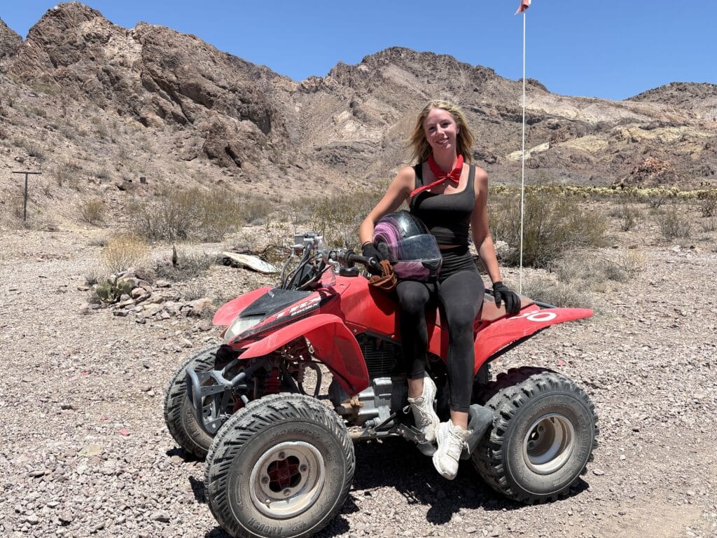 Smiling woman in black activewear on a red ATV in Nevada desert near Las Vegas during thrilling ATV tour with mountain views.
