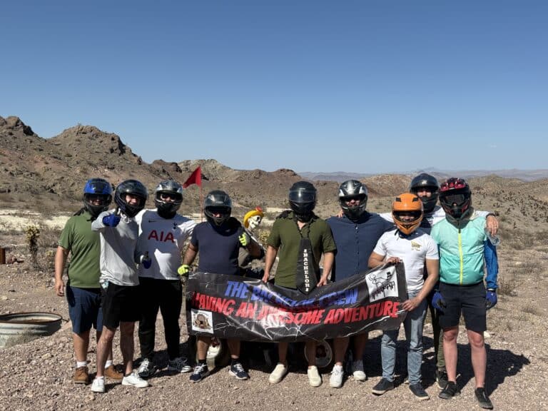 Nine helmeted adventurers pose in Nevada’s desert near Las Vegas, holding a Team Adventure banner after an ATV tour.