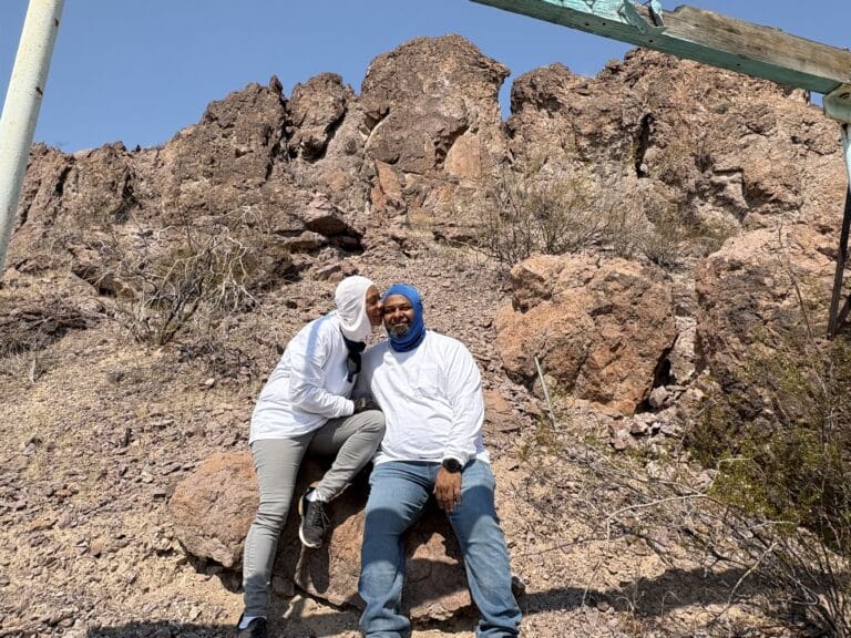 Two people in white shirts rest on desert rocks near Las Vegas, Nevada, perfect for ATV tours or Ghost Town sightseeing.