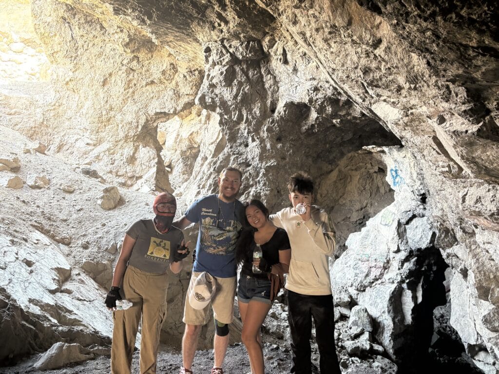 Four friends smile in a Nevada cave near the Colorado River, lit by sunlight during a Las Vegas ATV tour adventure.
