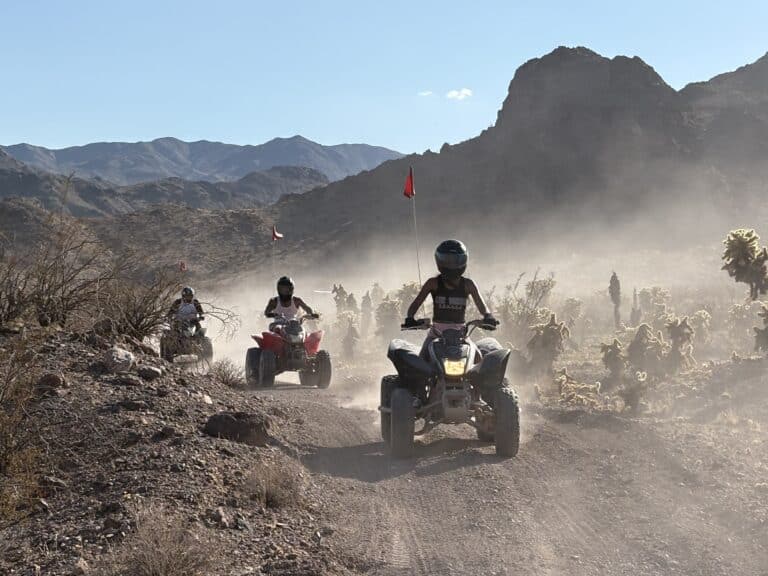 Adventurers enjoy an ATV tour near Las Vegas, Nevada, riding dusty desert trails by rocky mountains and sparse desert scenery.