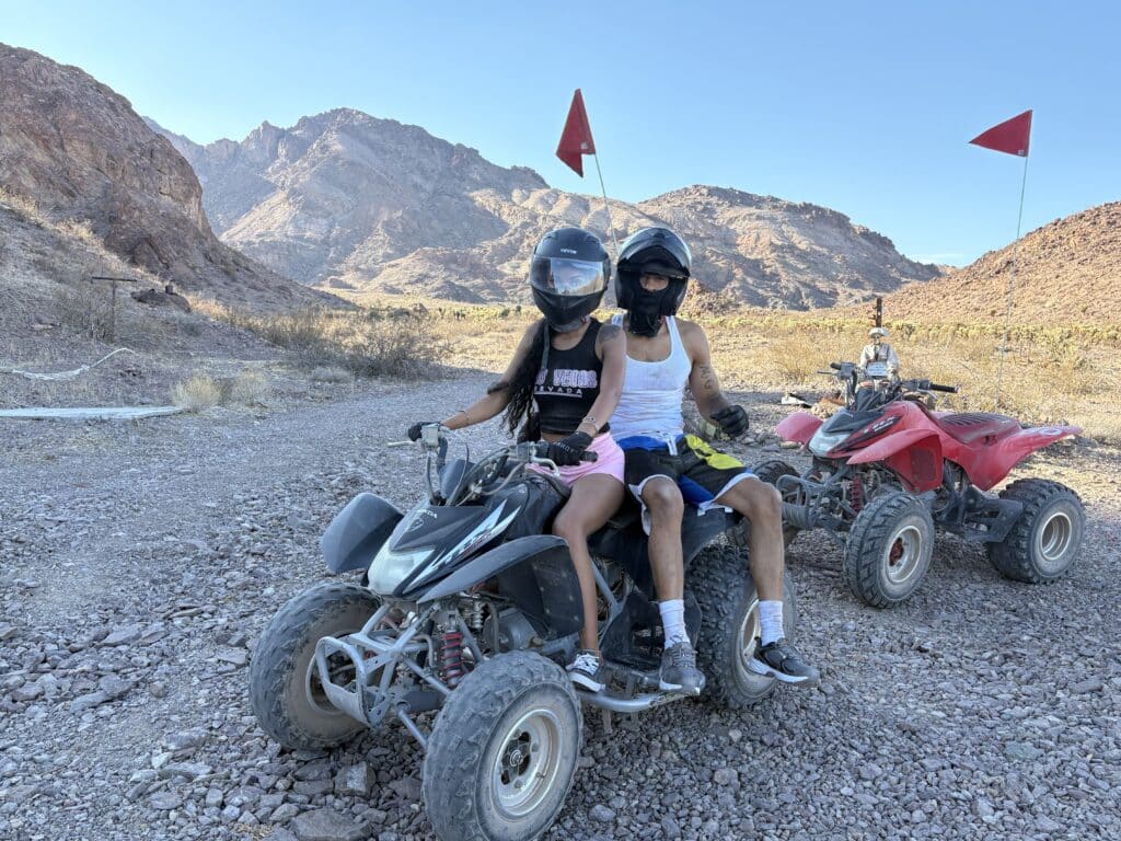 Two riders in helmets on an ATV in the Nevada desert near Las Vegas, with RZR off-road tours by the Colorado River and Ghost Towns.