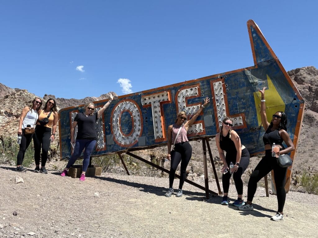 Six women in activewear smile by a vintage MOTEL sign near Las Vegas, Nevada, after RZR off-road rides by the Colorado River.