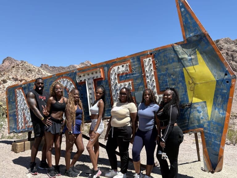 Eight friends smile by a vintage MOTEL sign in Nevadas desert near Las Vegas, perfect for ATV tours & Ghost Town adventures.