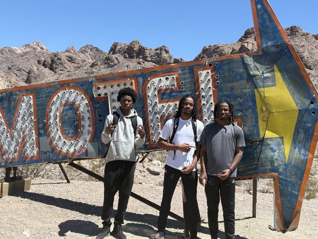 Three men pose by a vintage MOTEL sign near Nevada’s rocky desert, close to Las Vegas and the Colorado River—ideal for ATV tours.