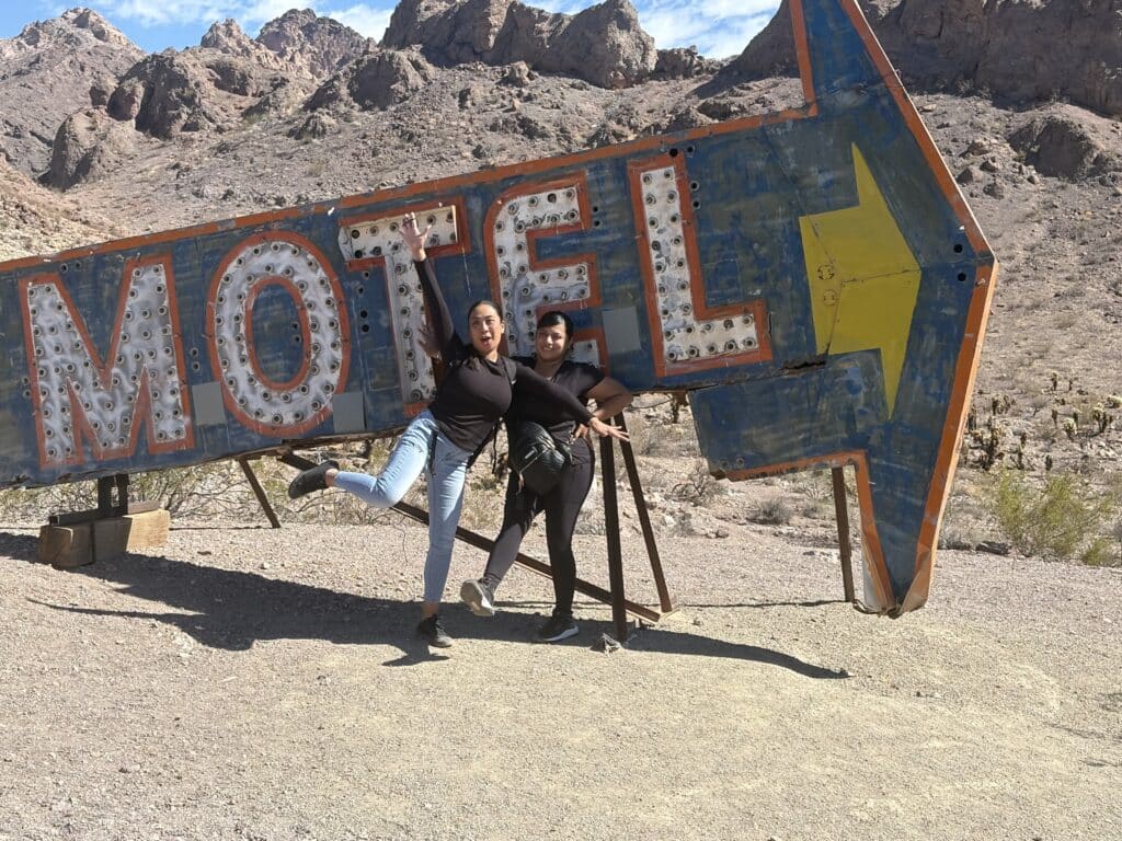 Two friends pose by a vintage MOTEL sign near Las Vegas, Nevada—perfect for Ghost Town sightseeing & Colorado River ATV tours.