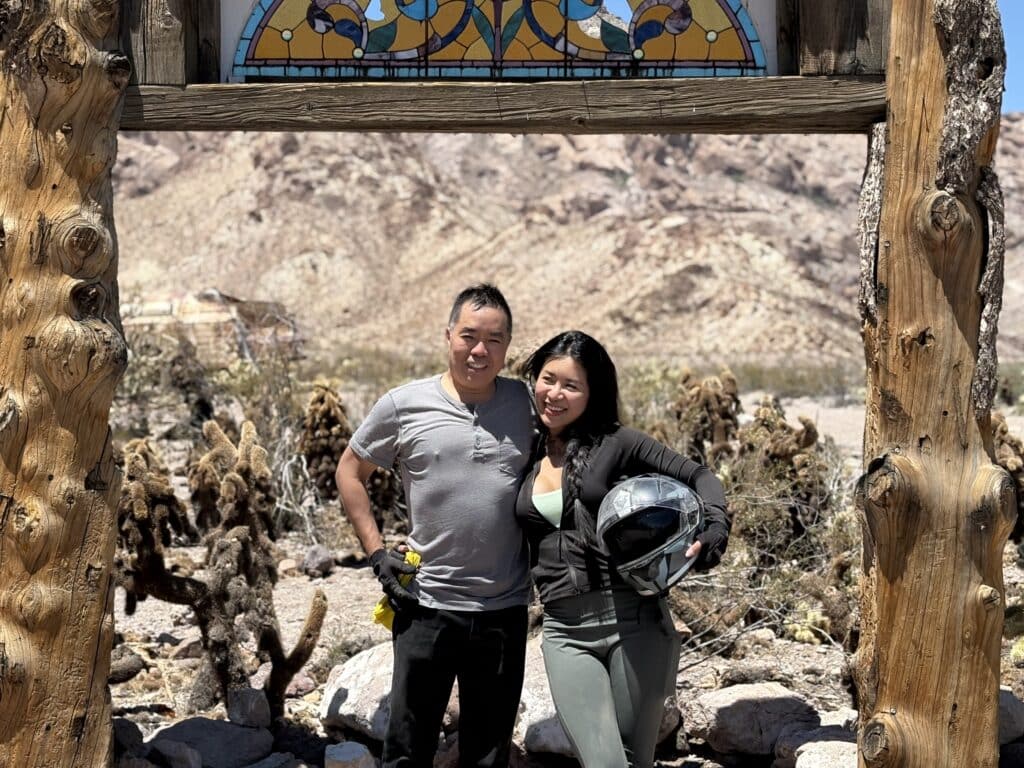 A couple smiles under a wooden arch in the Nevada desert near Las Vegas, ready for ATV tours with mountains and cacti behind them.