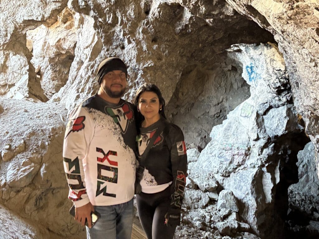 Smiling couple in matching motocross jerseys inside a sunlit Nevada cave near Las Vegas on an ATV tour along the Colorado River.