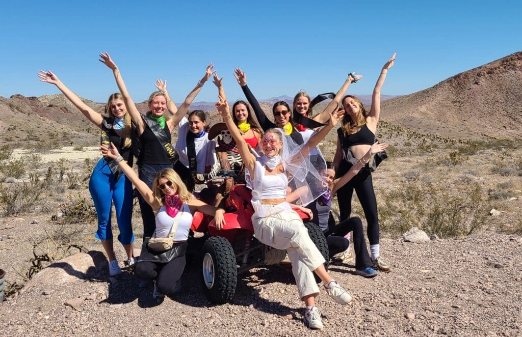 Ten women celebrate atop an ATV in the Nevada desert on a Las Vegas ATV tour near the Colorado River under blue skies.