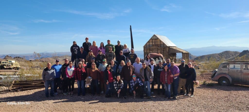 A group enjoys a Las Vegas ATV tour near the Colorado River, posing by vintage cars & a ghost town in Nevada’s scenic desert hills.