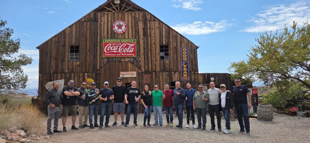 Sixteen friends smile in front of a vintage Nevada building after an epic Las Vegas ATV tour and Ghost Town adventure by the Colorado River.