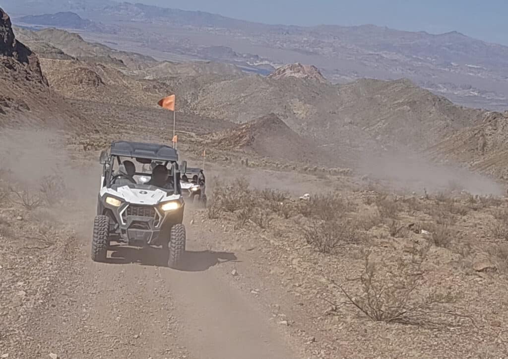 Two RZRs with orange flags kick up dust on a Nevada desert trail near Las Vegas, perfect for ATV tours and Colorado River adventures.