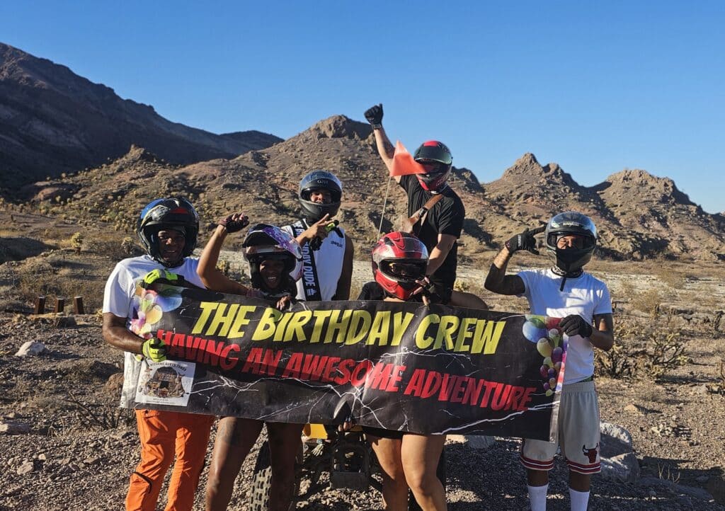 Five friends in helmets celebrate with a banner before an epic ATV tour near Las Vegas & the Colorado River, Nevada desert adventure!.