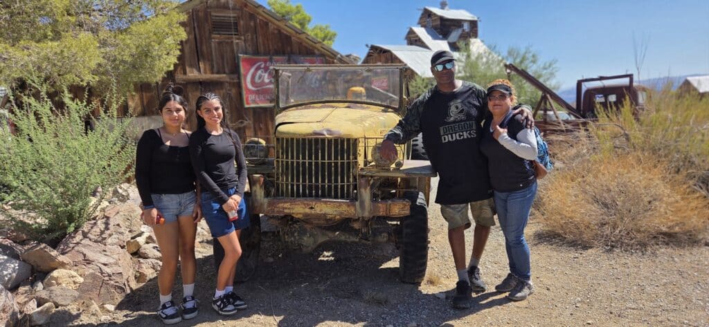 Four friends pose by a rusty yellow truck in a Nevada ghost town near Las Vegas—perfect for ATV tours and Colorado River adventures.