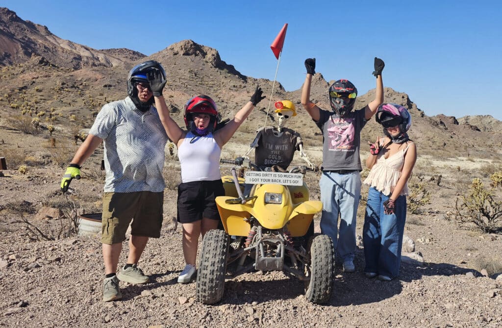 Adventure-seekers in helmets celebrate beside a yellow ATV during an exciting Nevada desert tour near Las Vegas and the Colorado River.